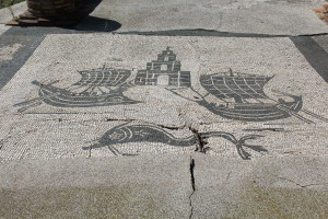 Mosaic that could be depicting a vendor that unloads and transports goods in the harbor. The flat lines indicate the calm waters of a harbor with a lighthouse in the background.